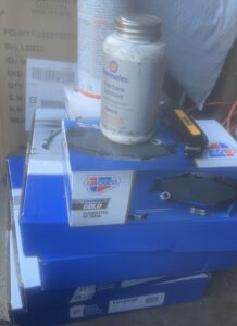 Stack of automotive parts boxes with brake pads and a container of automotive grease, representing mobile mechanic services at Steve's Pit Stop Mobile Mechanic.