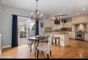 Modern kitchen and dining area featuring a round table with a decorative plate, a patterned chair, and a chandelier, with sliding glass doors leading to an outdoor space.